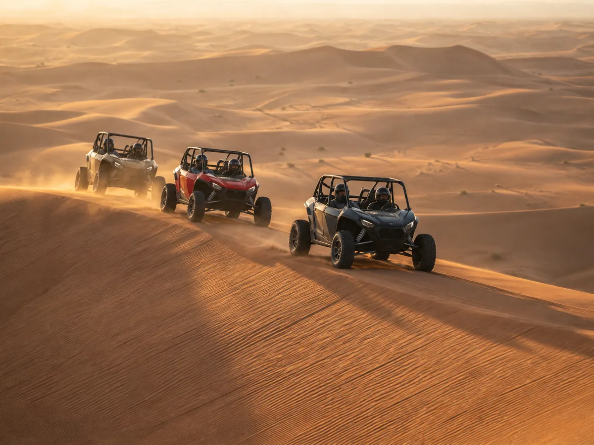 Three side-by-side buggies in a guided convoy along the crest of a red dune ridge in the Dubai desert